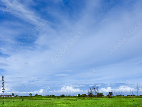 blue sky with white fluffy clouds and grass field near village