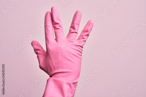Hand of caucasian young man with cleaning glove over isolated pink background greeting doing Vulcan salute  showing back of the hand and fingers  freak culture