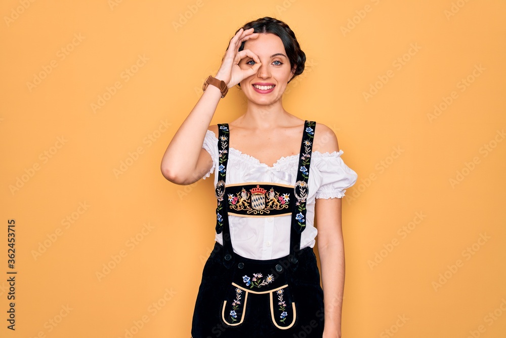 Young beautiful german woman with blue eyes wearing traditional octoberfest dress doing ok gesture with hand smiling, eye looking through fingers with happy face. Young beautiful german woman with blue eyes wearing traditional octoberfest dress doing ok gesture with hand smiling, eye looking through fingers with happy face.