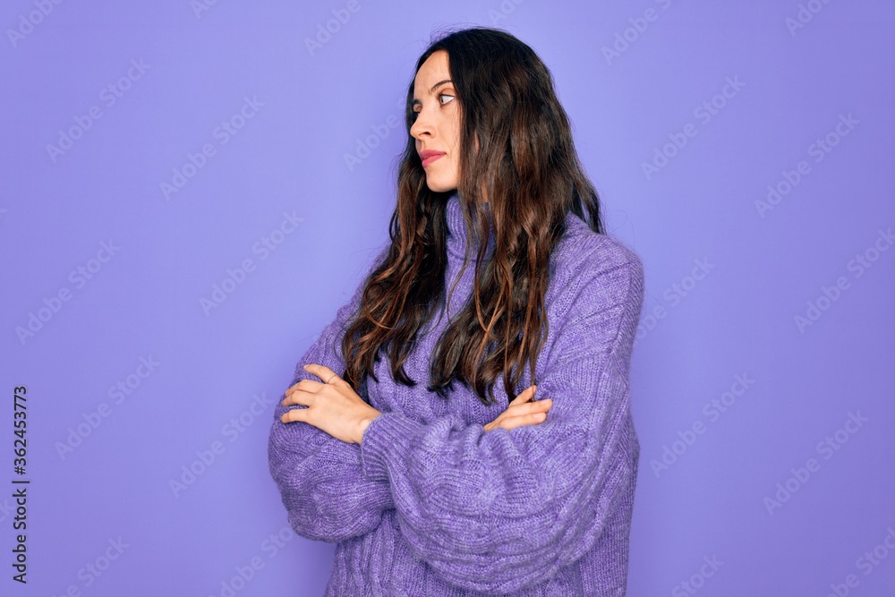 Fototapeta premium Young beautiful woman wearing casual turtleneck sweater standing over purple background looking to the side with arms crossed convinced and confident