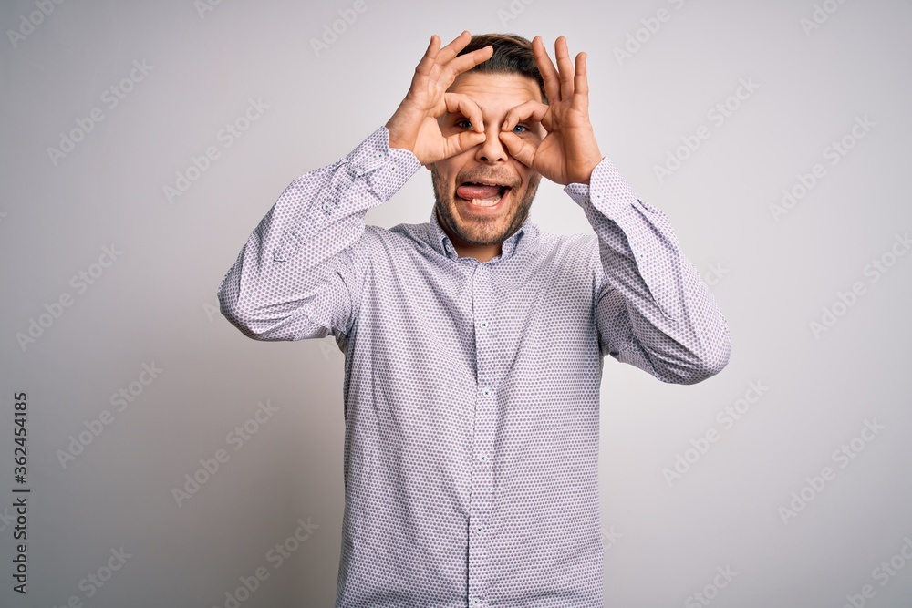 Young business man with blue eyes standing over isolated background doing ok gesture like binoculars sticking tongue out, eyes looking through fingers. Crazy expression. Young business man with blue eyes standing over isolated background doing ok gesture like binoculars sticking tongue out, eyes looking through fingers. Crazy expression.