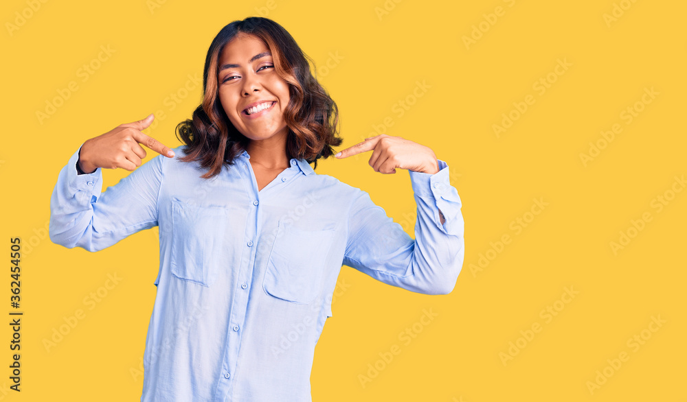 Young beautiful mixed race woman wearing casual business shirt looking confident with smile on face, pointing oneself with fingers proud and happy. Young beautiful mixed race woman wearing casual business shirt looking confident with smile on face, pointing oneself with fingers proud and happy.
