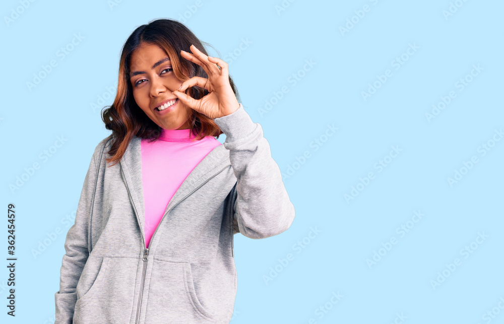 Young beautiful mixed race woman wearing casual sporty clothes smiling positive doing ok sign with hand and fingers. successful expression. Young beautiful mixed race woman wearing casual sporty clothes smiling positive doing ok sign with hand and fingers. successful expression.