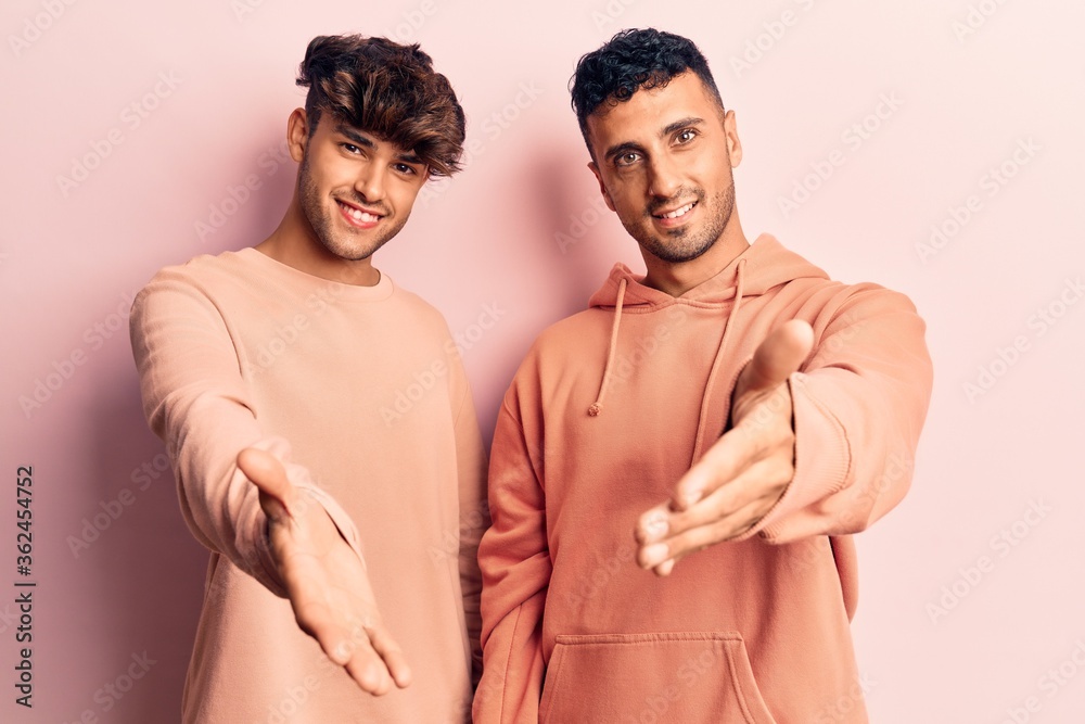 Young gay couple wearing casual clothes smiling cheerful offering palm hand giving assistance and acceptance. Young gay couple wearing casual clothes smiling cheerful offering palm hand giving assistance and acceptance.