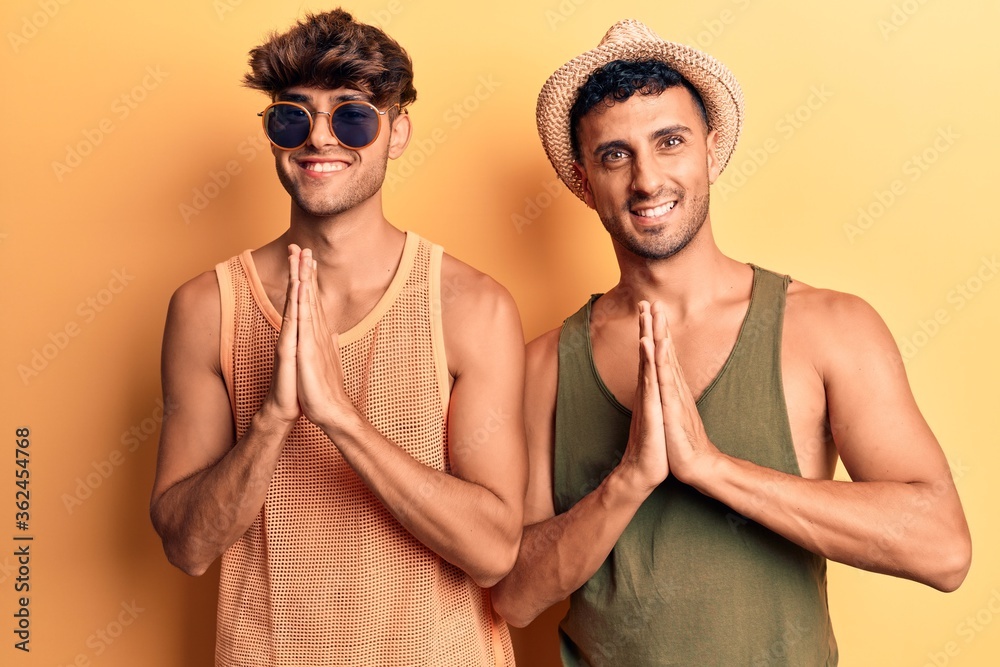 Young gay couple wearing summer clothes praying with hands together asking for forgiveness smiling confident. Young gay couple wearing summer clothes praying with hands together asking for forgiveness smiling confident.