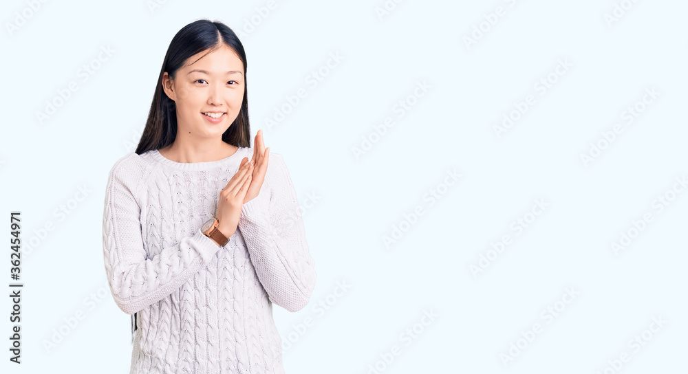 Young beautiful chinese woman wearing casual sweater clapping and applauding happy and joyful, smiling proud hands together Young beautiful chinese woman wearing casual sweater clapping and applauding happy and joyful, smiling proud hands together
