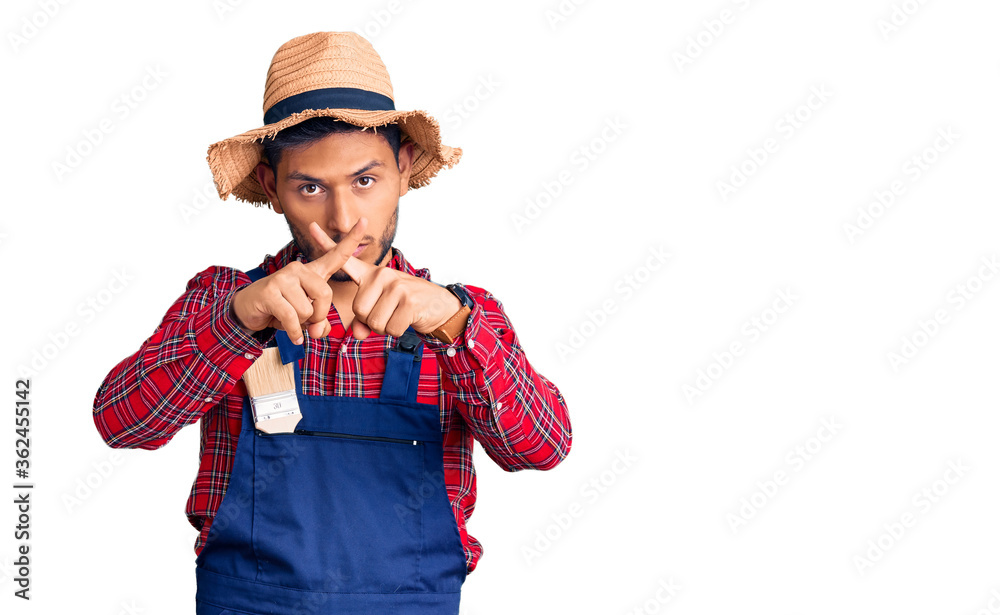 Handsome latin american young man weaing handyman uniform rejection expression crossing fingers doing negative sign Handsome latin american young man weaing handyman uniform rejection expression crossing fingers doing negative sign