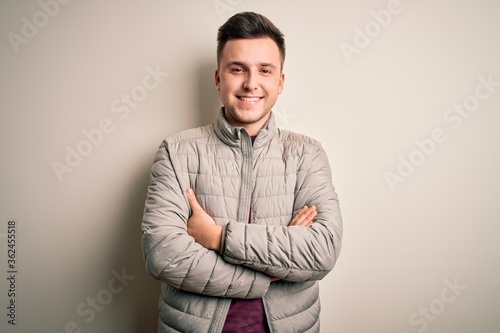 Young handsome caucasian man wearing casual winter jacket standing over isolated background happy face smiling with crossed arms looking at the camera. Positive person. © Krakenimages.com
