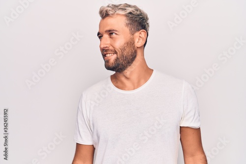 Young handsome blond man wearing casual t-shirt standing over isolated white background looking to side, relax profile pose with natural face and confident smile.