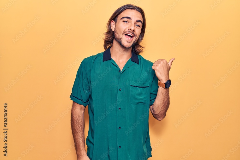 Young handsome man wearing casual clothes pointing thumb up to the side smiling happy with open mouth Young handsome man wearing casual clothes pointing thumb up to the side smiling happy with open mouth