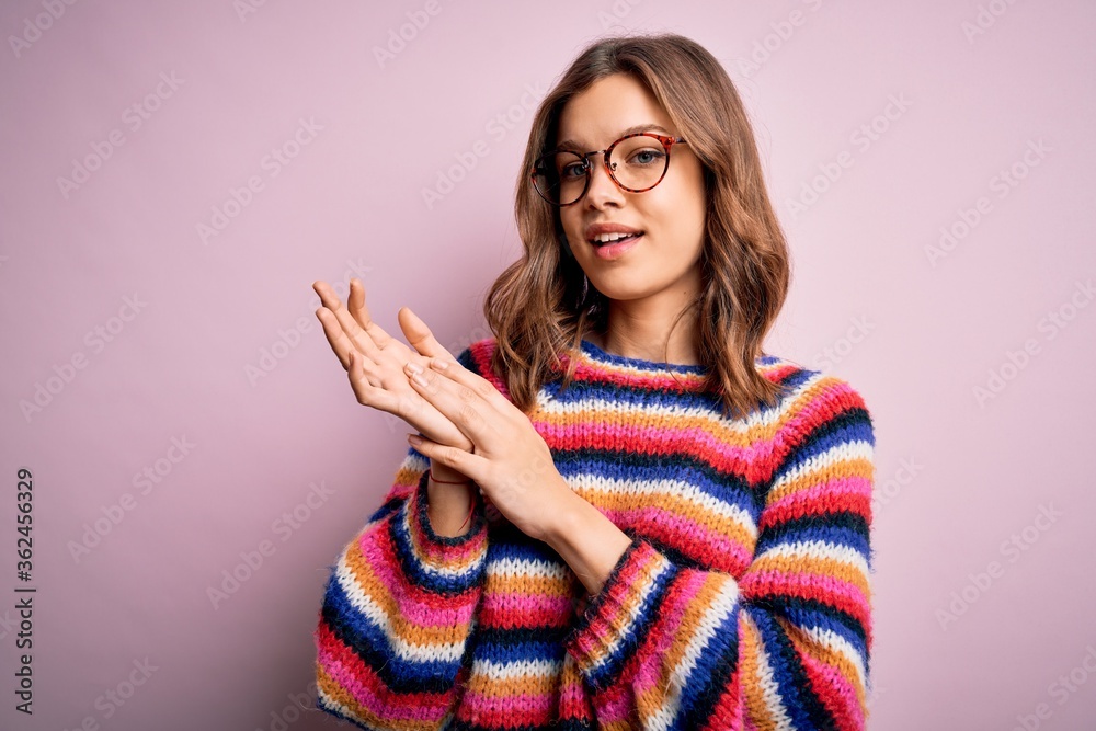 Young beautiful blonde girl wearing glasses and casual sweater over pink isolated background clapping and applauding happy and joyful, smiling proud hands together Young beautiful blonde girl wearing glasses and casual sweater over pink isolated background clapping and applauding happy and joyful, smiling proud hands together