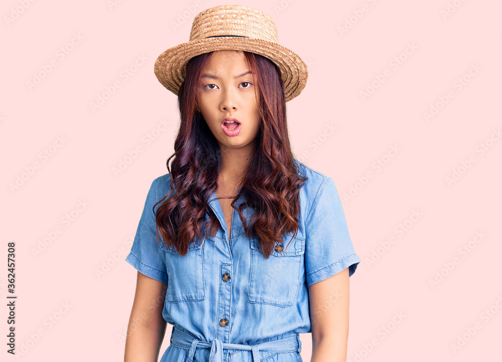 Young beautiful chinese girl wearing summer hat in shock face, looking skeptical and sarcastic, surprised with open mouth Young beautiful chinese girl wearing summer hat in shock face, looking skeptical and sarcastic, surprised with open mouth