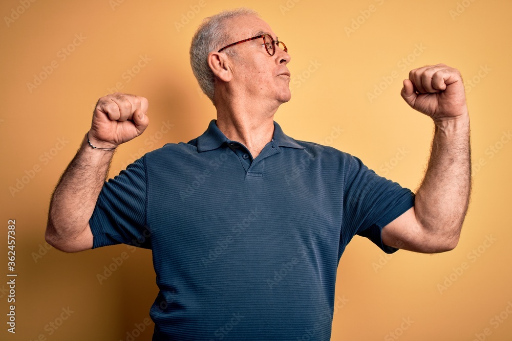 Middle age handsome hoary man wearing casual polo and glasses over yellow background showing arms muscles smiling proud. Fitness concept. Middle age handsome hoary man wearing casual polo and glasses over yellow background showing arms muscles smiling proud. Fitness concept.