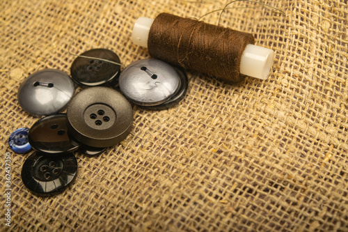 Different buttons and a spool of thread on the burlap with a rough texture. Close up.
