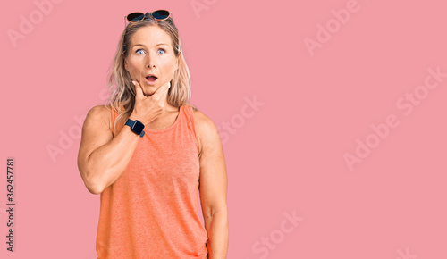 Middle age fit blonde woman wearing casual summer clothes and sunglasses looking fascinated with disbelief, surprise and amazed expression with hands on chin
