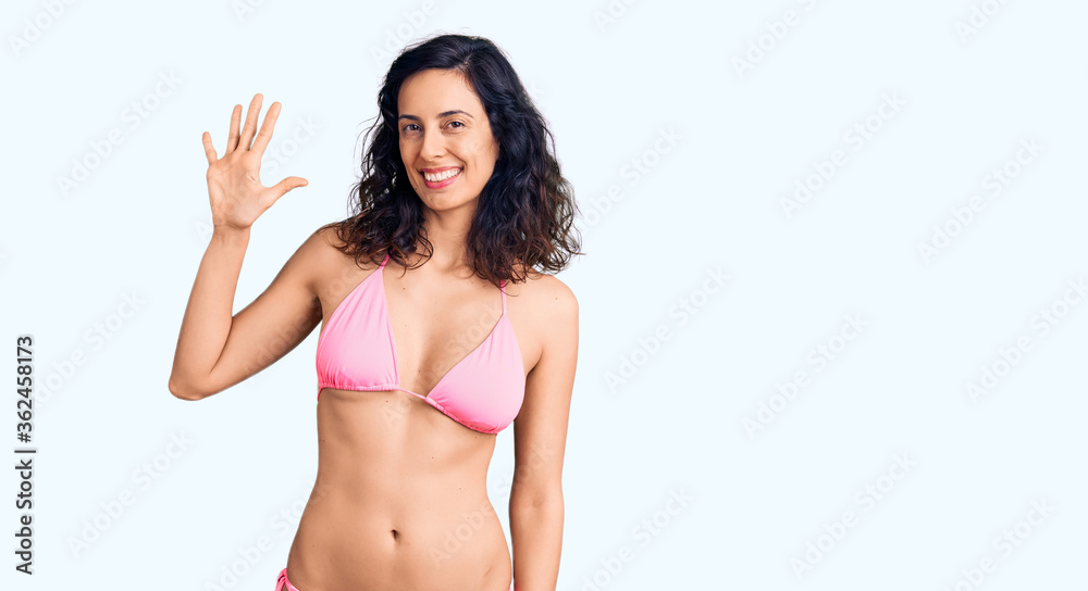 Young beautiful hispanic woman wearing bikini showing and pointing up with fingers number five while smiling confident and happy. Young beautiful hispanic woman wearing bikini showing and pointing up with fingers number five while smiling confident and happy.