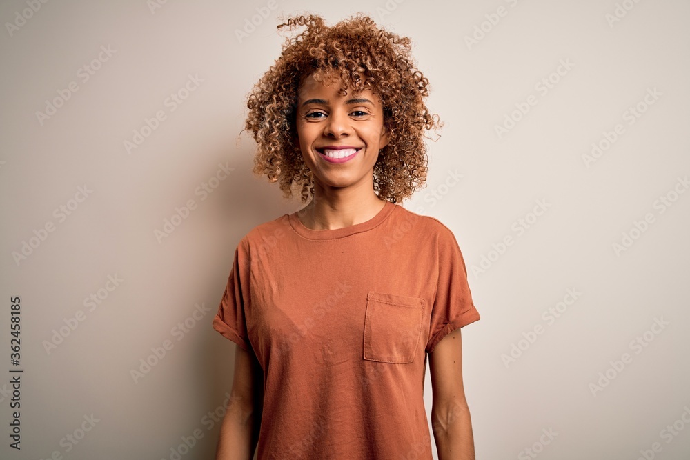 Beautiful african american woman with curly hair wearing casual t-shirt over white background with a happy and cool smile on face. Lucky person.