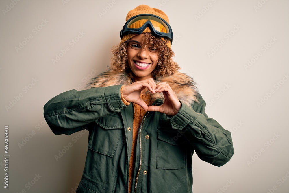 Young african american skier woman with curly hair wearing snow sportswear and ski goggles smiling in love doing heart symbol shape with hands. Romantic concept. Young african american skier woman with curly hair wearing snow sportswear and ski goggles smiling in love doing heart symbol shape with hands. Romantic concept.