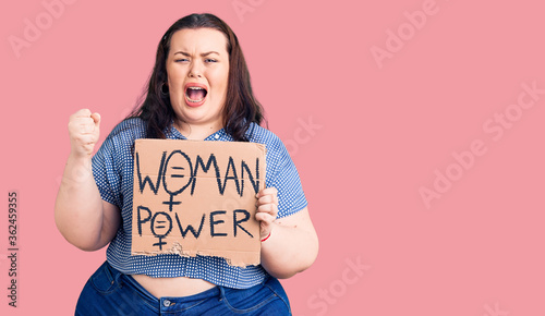 Young plus size woman holding woman power banner annoyed and frustrated shouting with anger, yelling crazy with anger and hand raised photo