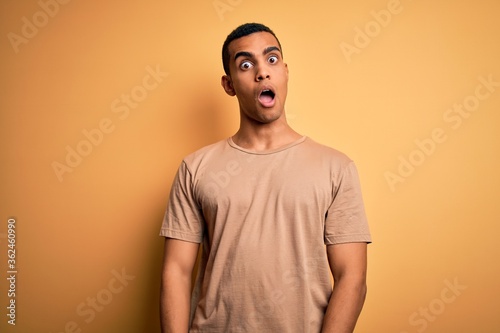 Young handsome african american man wearing casual t-shirt standing over yellow background In shock face, looking skeptical and sarcastic, surprised with open mouth