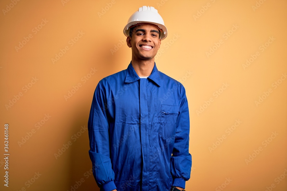 Young handsome african american worker man wearing blue uniform and security helmet with a happy and cool smile on face. Lucky person.