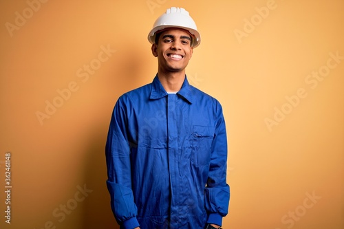 Young handsome african american worker man wearing blue uniform and security helmet with a happy and cool smile on face. Lucky person. photo