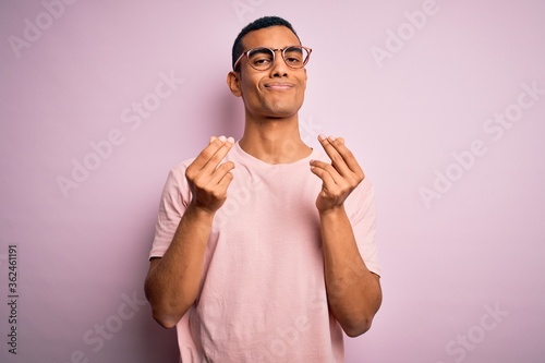 Handsome african american man wearing casual t-shirt and glasses over pink background doing money gesture with hands, asking for salary payment, millionaire business © Krakenimages.com