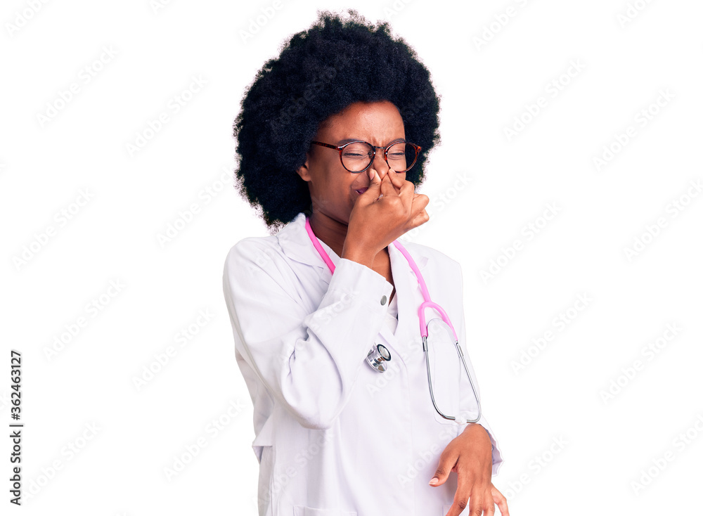 Young african american woman wearing doctor coat and stethoscope smelling something stinky and disgusting, intolerable smell, holding breath with fingers on nose. bad smell Young african american woman wearing doctor coat and stethoscope smelling something stinky and disgusting, intolerable smell, holding breath with fingers on nose. bad smell