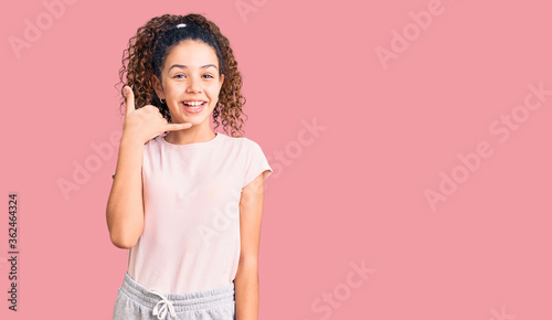 Beautiful kid girl with curly hair wearing casual clothes smiling doing phone gesture with hand and fingers like talking on the telephone. communicating concepts.
