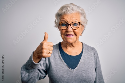 Senior beautiful grey-haired woman wearing casual sweater and glasses over white background doing happy thumbs up gesture with hand. Approving expression looking at the camera showing success.