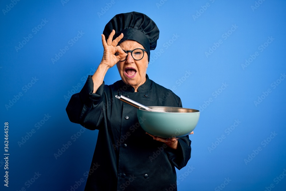 Senior beautiful grey-haired chef woman wearing cooker uniform and hat using whisk and bowl with happy face smiling doing ok sign with hand on eye looking through fingers Senior beautiful grey-haired chef woman wearing cooker uniform and hat using whisk and bowl with happy face smiling doing ok sign with hand on eye looking through fingers