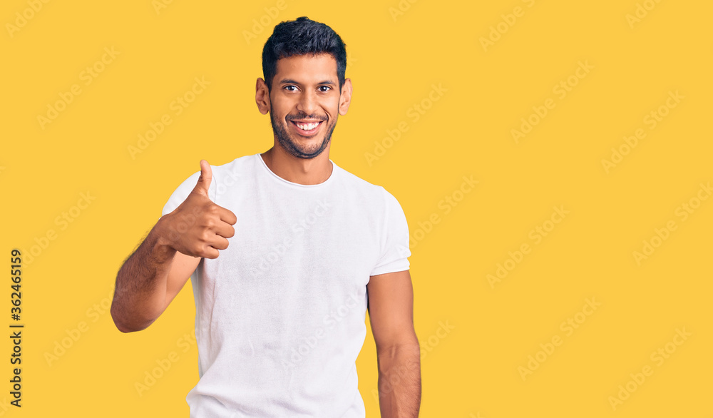 Young latin man wearing casual clothes doing happy thumbs up gesture with hand. approving expression looking at the camera showing success. Young latin man wearing casual clothes doing happy thumbs up gesture with hand. approving expression looking at the camera showing success.