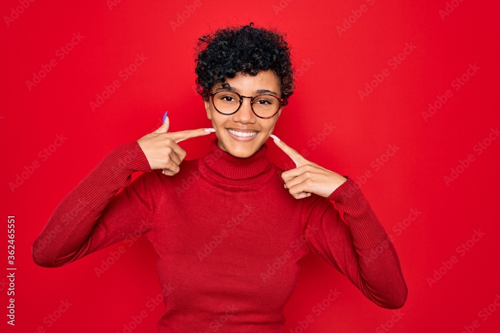 Young beautiful african american afro woman wearing turtleneck sweater and glasses smiling cheerful showing and pointing with fingers teeth and mouth. Dental health concept. Young beautiful african american afro woman wearing turtleneck sweater and glasses smiling cheerful showing and pointing with fingers teeth and mouth. Dental health concept.