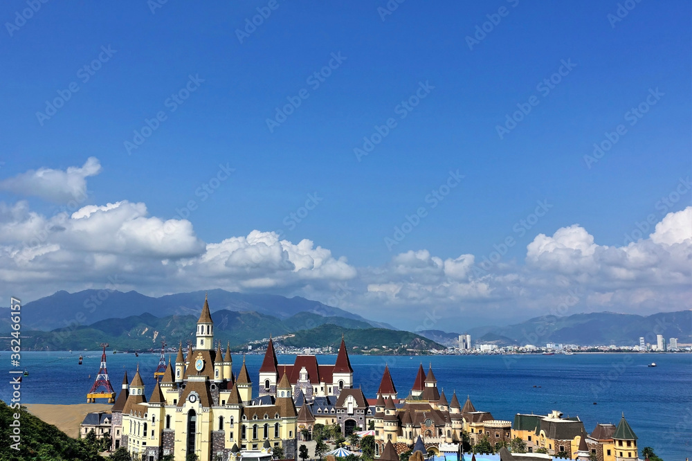 Vietnamese landscape. In the foreground is a castle for children's games, a cable car through the bay. In the distance are mountains, silhouettes of urban buildings, a blue sky with picturesque clouds