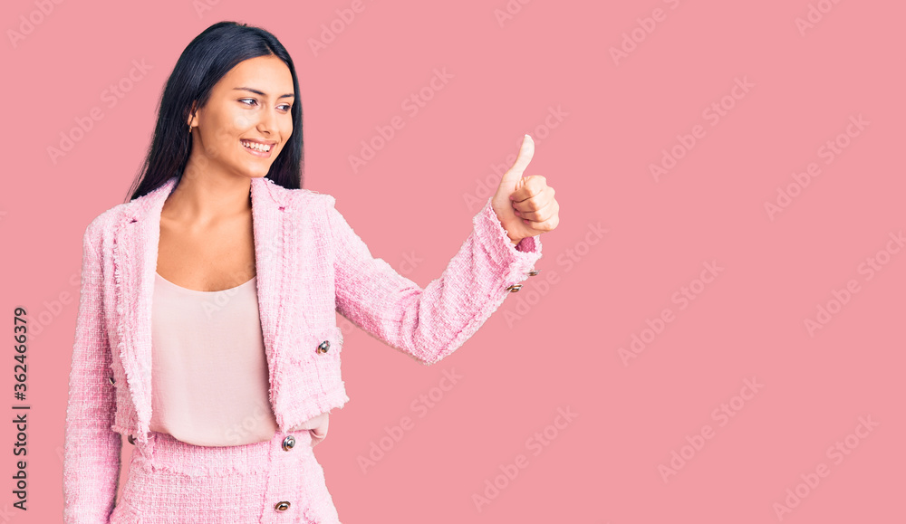 Young beautiful latin girl wearing business clothes looking proud, smiling doing thumbs up gesture to the side Young beautiful latin girl wearing business clothes looking proud, smiling doing thumbs up gesture to the side