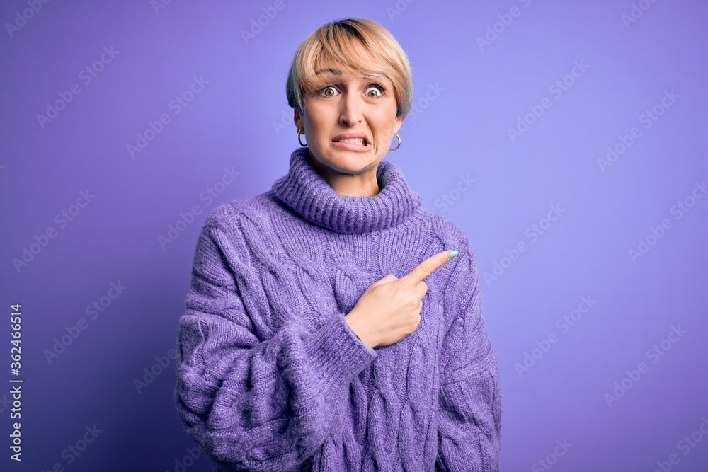 Young blonde woman with short hair wearing winter turtleneck sweater over purple background Pointing aside worried and nervous with forefinger, concerned and surprised expression Young blonde woman with short hair wearing winter turtleneck sweater over purple background Pointing aside worried and nervous with forefinger, concerned and surprised expression
