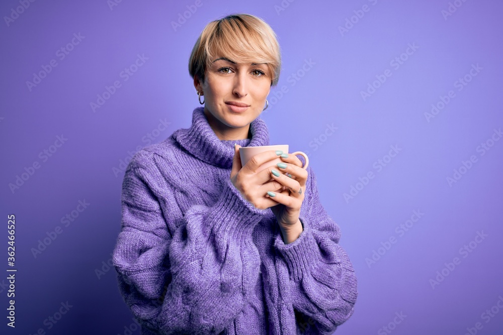 Young blonde woman with short hair wearing winter sweater drinking a cup of hot coffee with a confident expression on smart face thinking serious Young blonde woman with short hair wearing winter sweater drinking a cup of hot coffee with a confident expression on smart face thinking serious