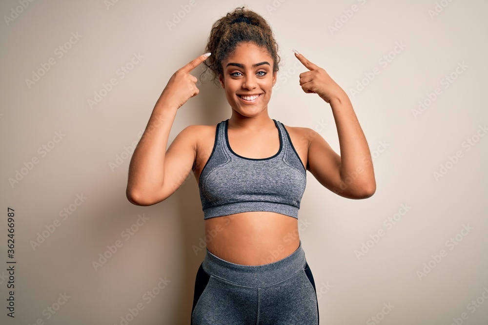 Young african american sportswoman doing sport wearing sportswear over white background smiling pointing to head with both hands finger, great idea or thought, good memory Young african american sportswoman doing sport wearing sportswear over white background smiling pointing to head with both hands finger, great idea or thought, good memory