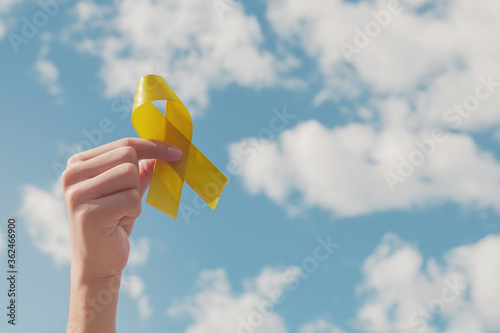 Hands holding yellow gold ribbon over blue sky, Sarcoma Awareness, Bone cancer, childhood cancer awareness, September yellow, World Suicide Prevention Day concept photo
