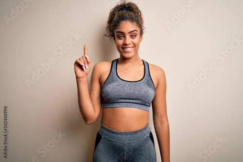 Young african american sportswoman doing sport wearing sportswear over white background showing and pointing up with finger number one while smiling confident and happy.