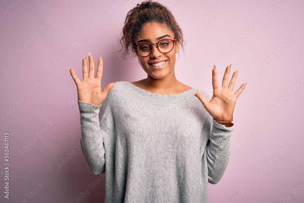 Young beautiful african american girl wearing sweater and glasses over pink background showing and pointing up with fingers number ten while smiling confident and happy. Young beautiful african american girl wearing sweater and glasses over pink background showing and pointing up with fingers number ten while smiling confident and happy.
