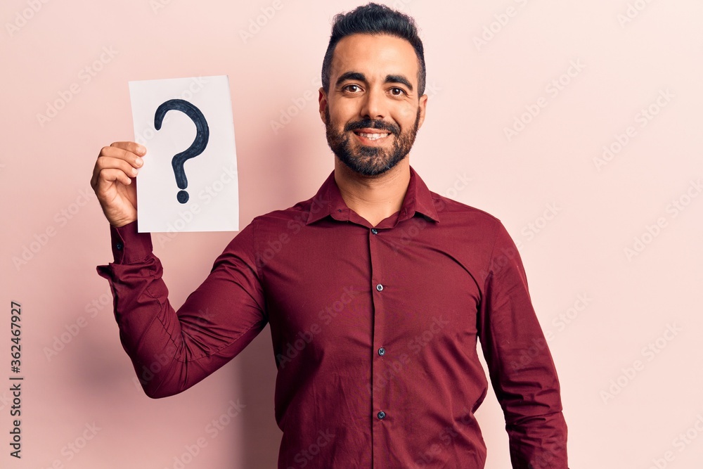 Young hispanic man holding question mark looking positive and happy standing and smiling with a confident smile showing teeth Young hispanic man holding question mark looking positive and happy standing and smiling with a confident smile showing teeth