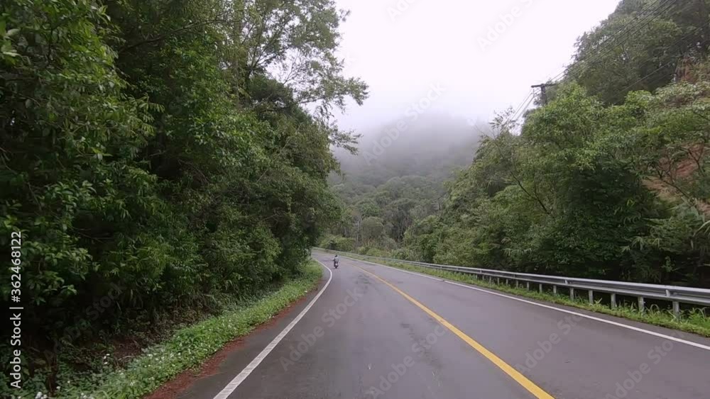 Driving on asphalt road with yellow markings passing through a tropical rain forest mountain with rain fog. Driving on asphalt road with yellow markings passing through a tropical rain forest mountain with rain fog.