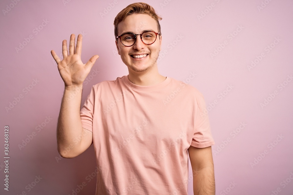 Young handsome redhead man wearing casual t-shirt standing over isolated pink background showing and pointing up with fingers number five while smiling confident and happy. Young handsome redhead man wearing casual t-shirt standing over isolated pink background showing and pointing up with fingers number five while smiling confident and happy.