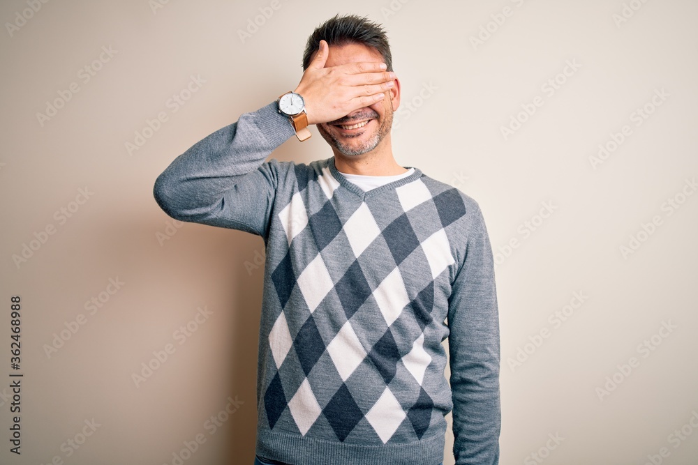 Young handsome man wearing casual sweater standing over isolated white background smiling and laughing with hand on face covering eyes for surprise. Blind concept. Young handsome man wearing casual sweater standing over isolated white background smiling and laughing with hand on face covering eyes for surprise. Blind concept.