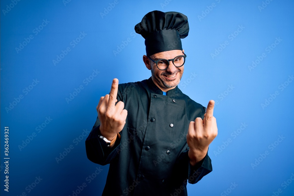 Young handsome chef man wearing cooker uniform and hat over isolated blue background Showing middle finger doing fuck you bad expression, provocation and rude attitude. Screaming excited Young handsome chef man wearing cooker uniform and hat over isolated blue background Showing middle finger doing fuck you bad expression, provocation and rude attitude. Screaming excited