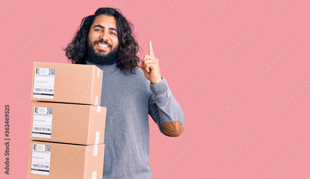 Young arab man holding delivery package surprised with an idea or question pointing finger with happy face, number one Young arab man holding delivery package surprised with an idea or question pointing finger with happy face, number one