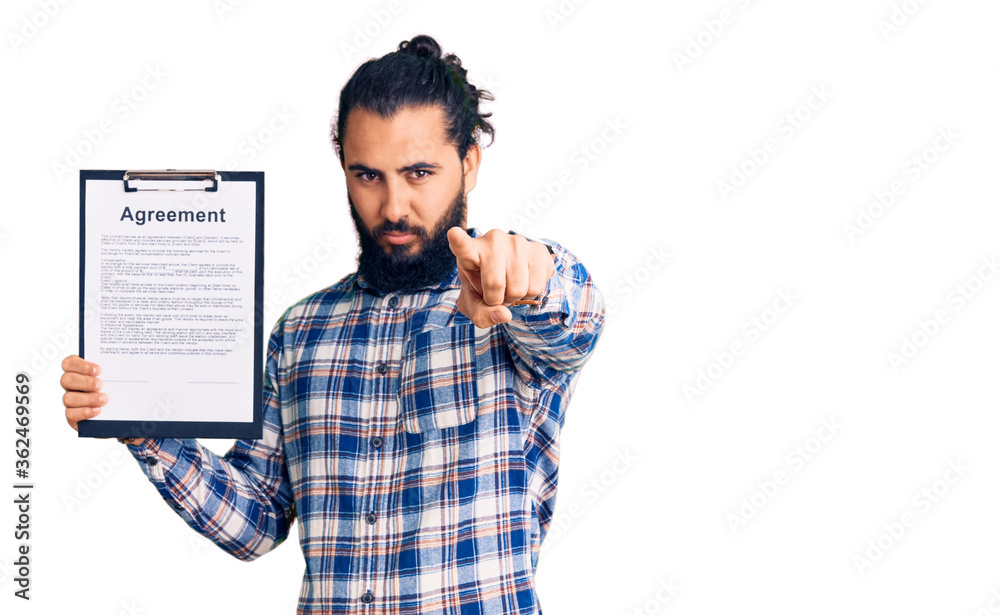 Young arab man holding clipboard with agreement document pointing with finger to the camera and to you, confident gesture looking serious Young arab man holding clipboard with agreement document pointing with finger to the camera and to you, confident gesture looking serious