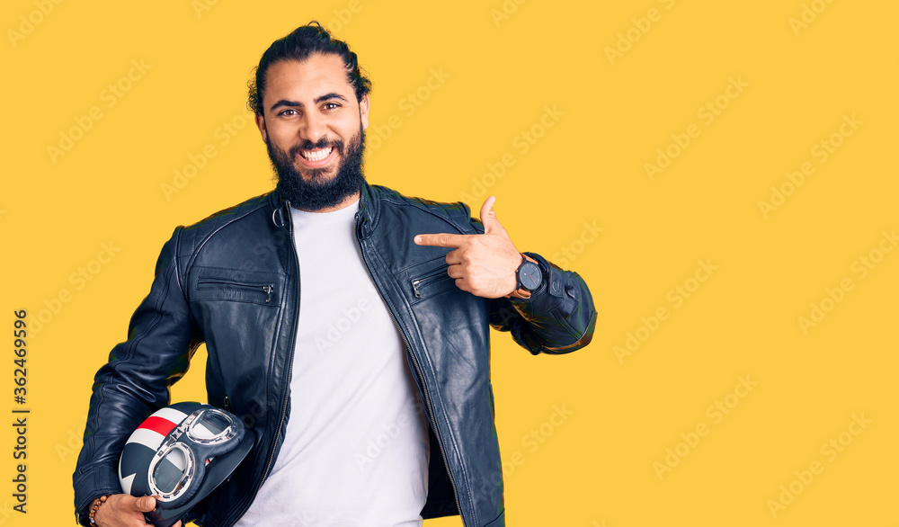 Young arab man holding motorcycle helmet pointing finger to one self smiling happy and proud Young arab man holding motorcycle helmet pointing finger to one self smiling happy and proud
