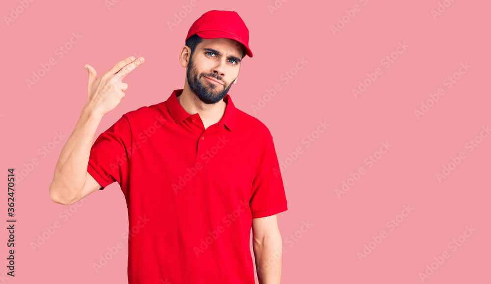 Young handsome man with beard wearing delivery uniform shooting and killing oneself pointing hand and fingers to head like gun, suicide gesture.